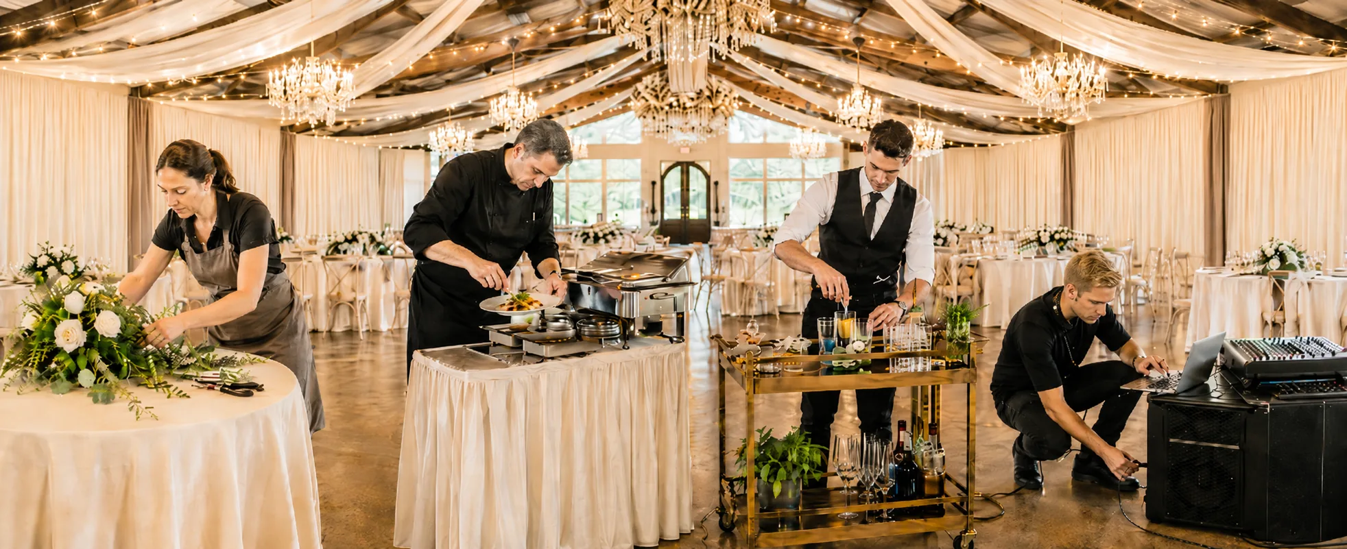 An outside florist, chef, bartender and DJ working side by side to set up a draped ballroom before a wedding reception at an open vendor venue near Houston